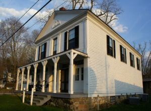 A large white building with many windows and a wrap-around porch.