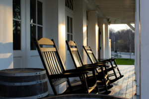 Three rocking chairs sit on the porch of a white building