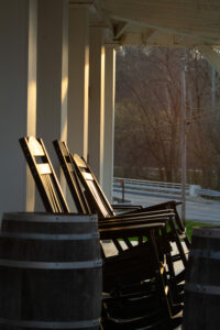 Rocking chairs sit on the porch of a white building at sunset