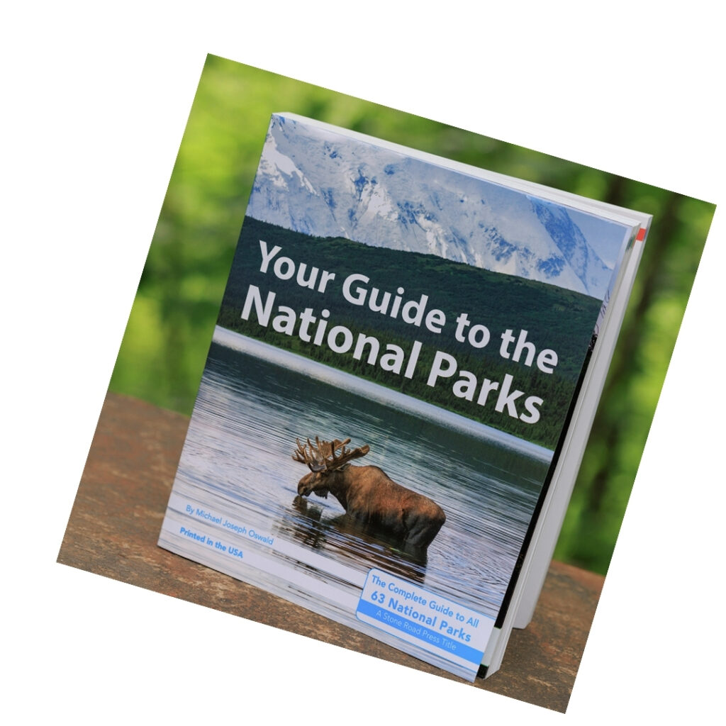 A photo of a book titled Your Guide to the National Parks. The cover illustration is of a moose standing in a lake with a mountain in the background. 