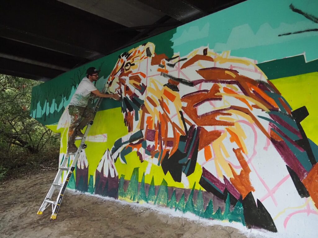 Arlin checking mural on ladder next to image of beaver.
